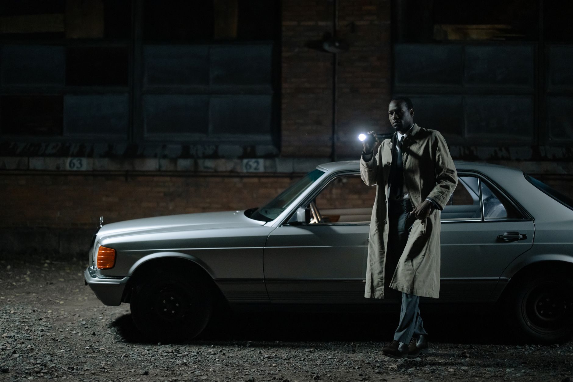 Detective conducting a night investigation by a car with a flashlight.