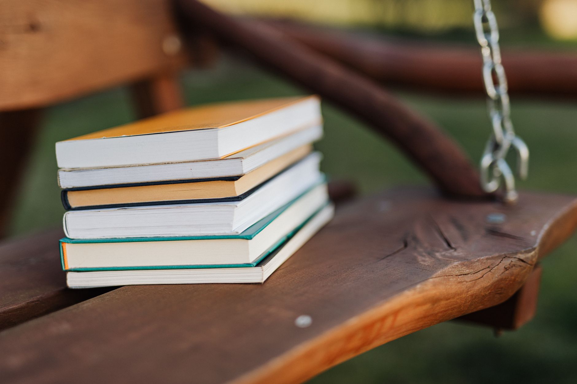 Pile of different books placed on brown wooden bench of swing in park