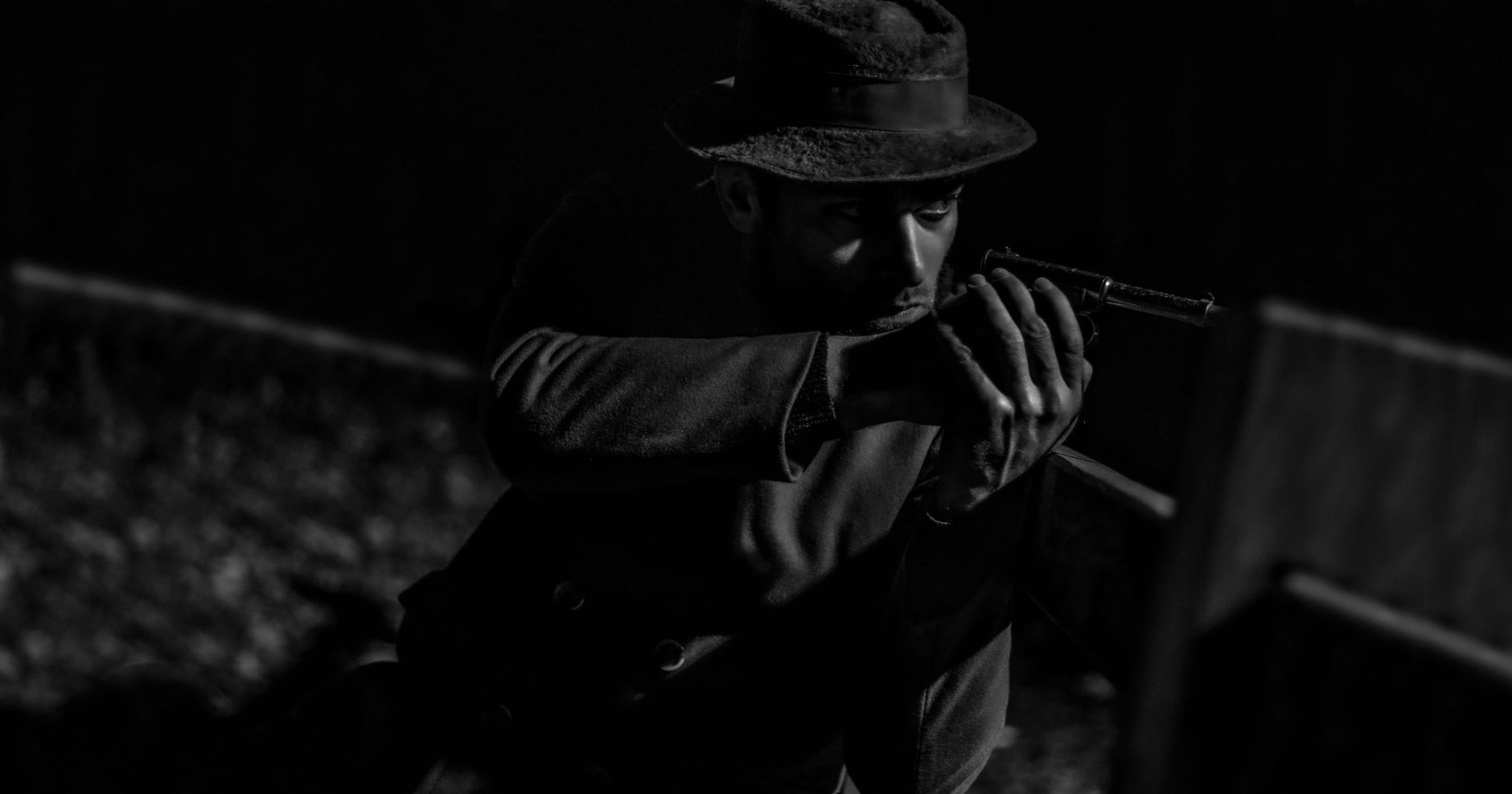 Mysterious man in noir style aiming a pistol with intense focus.