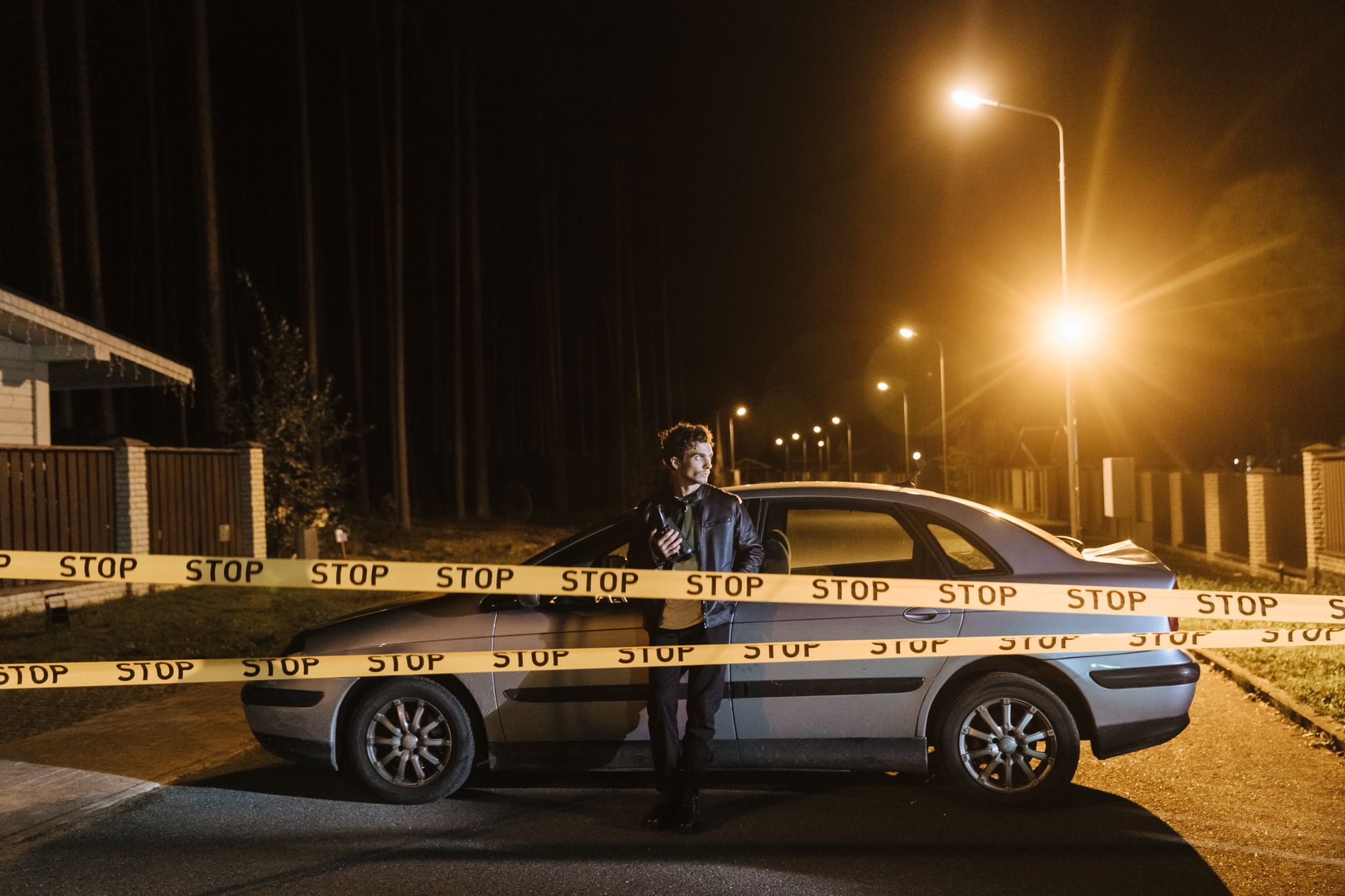 Man stands behind a car and stop tape at night, creating a mysterious scene.
