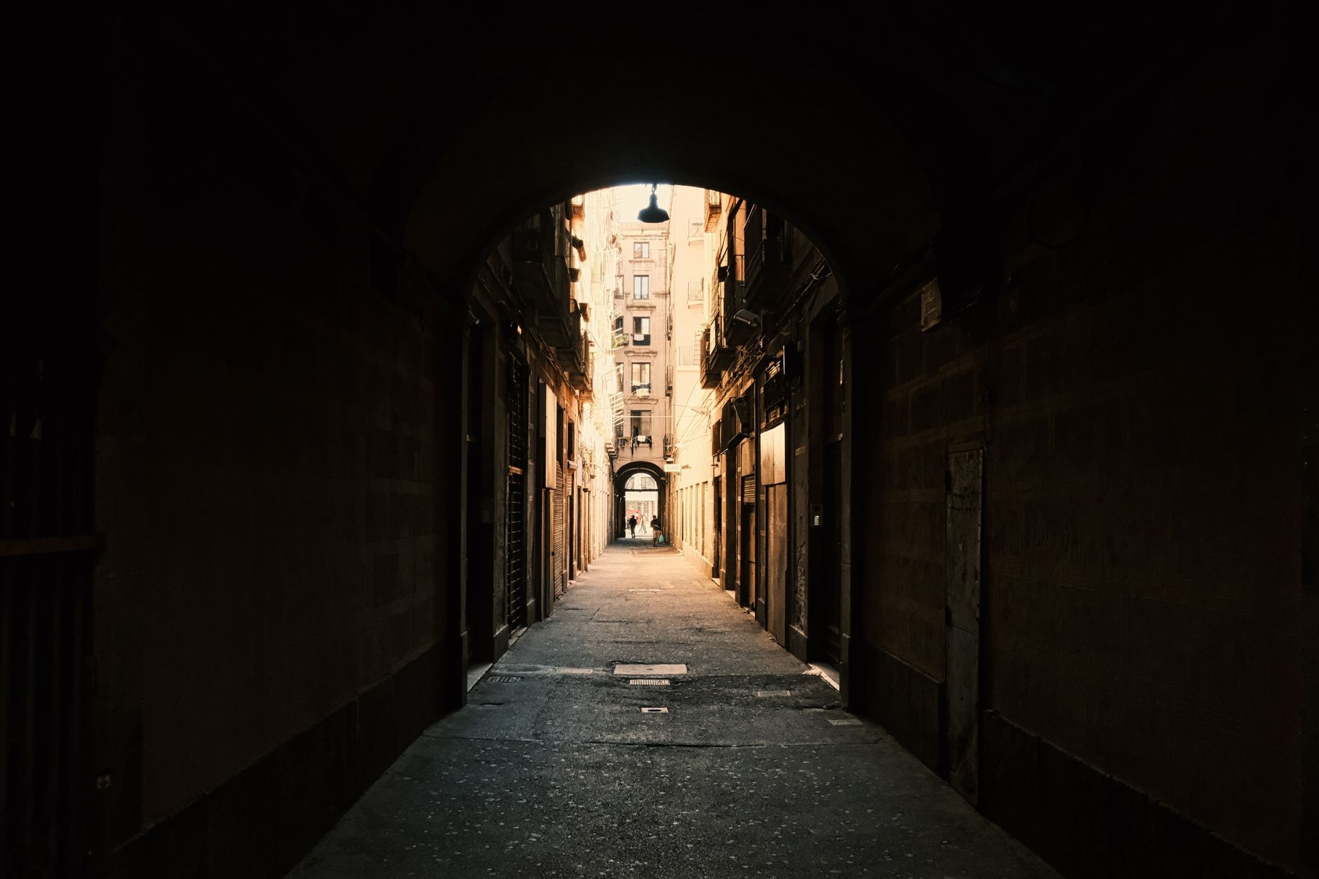 Explore the moody atmosphere of a narrow archway leading into a Barcelona alley, capturing a sense of mystery and urban architecture.