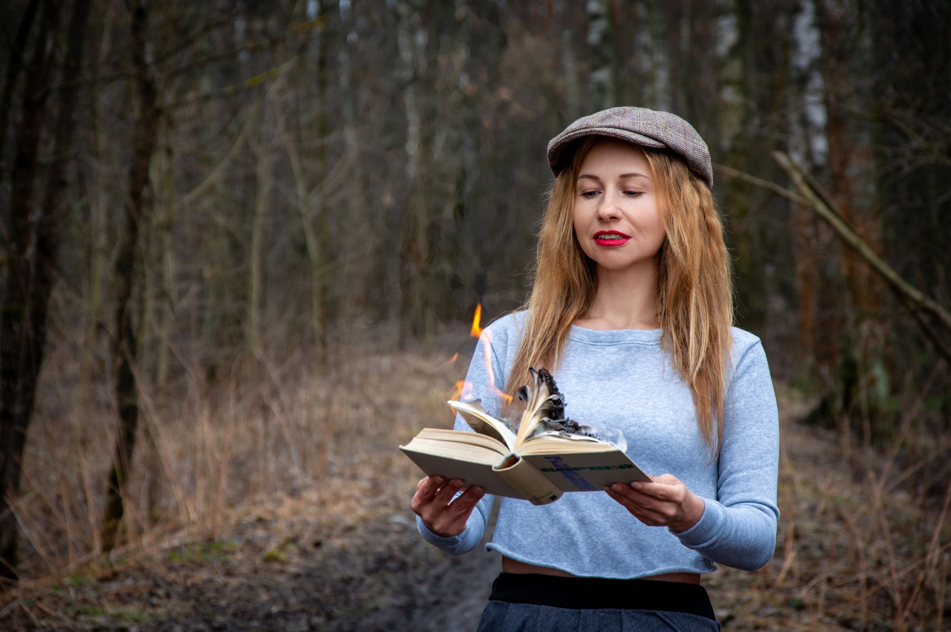 Woman reading a burning book in a forest shows dramatic tension and mystery.