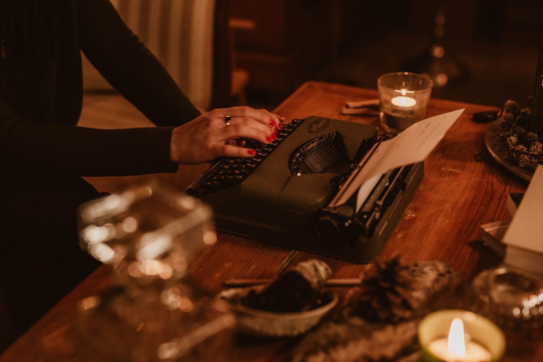 Close-up of hands typing on a vintage typewriter in a cozy, candle-lit setting.