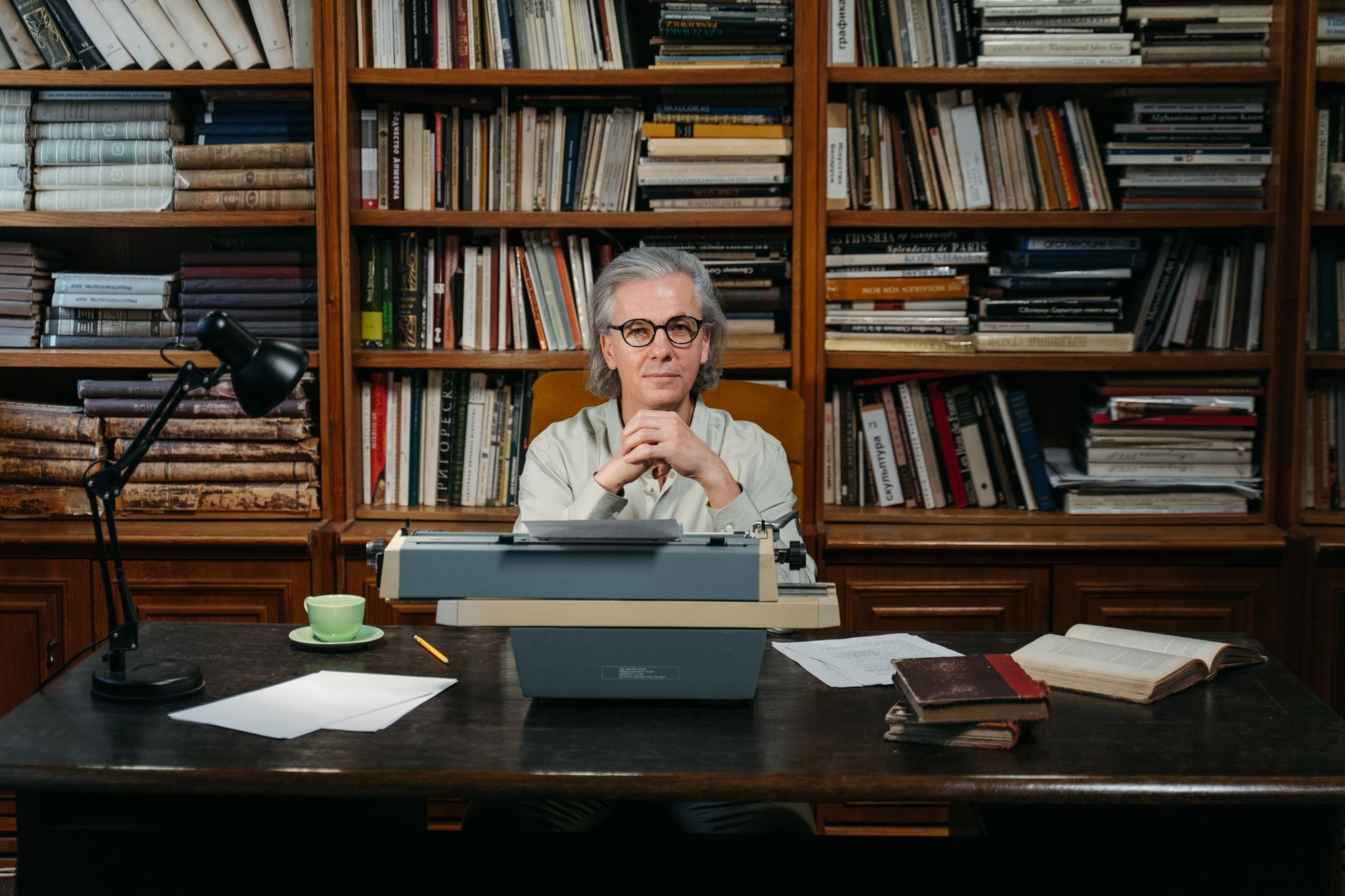 Senior man with typewriter in library, embodying wisdom and literary passion.