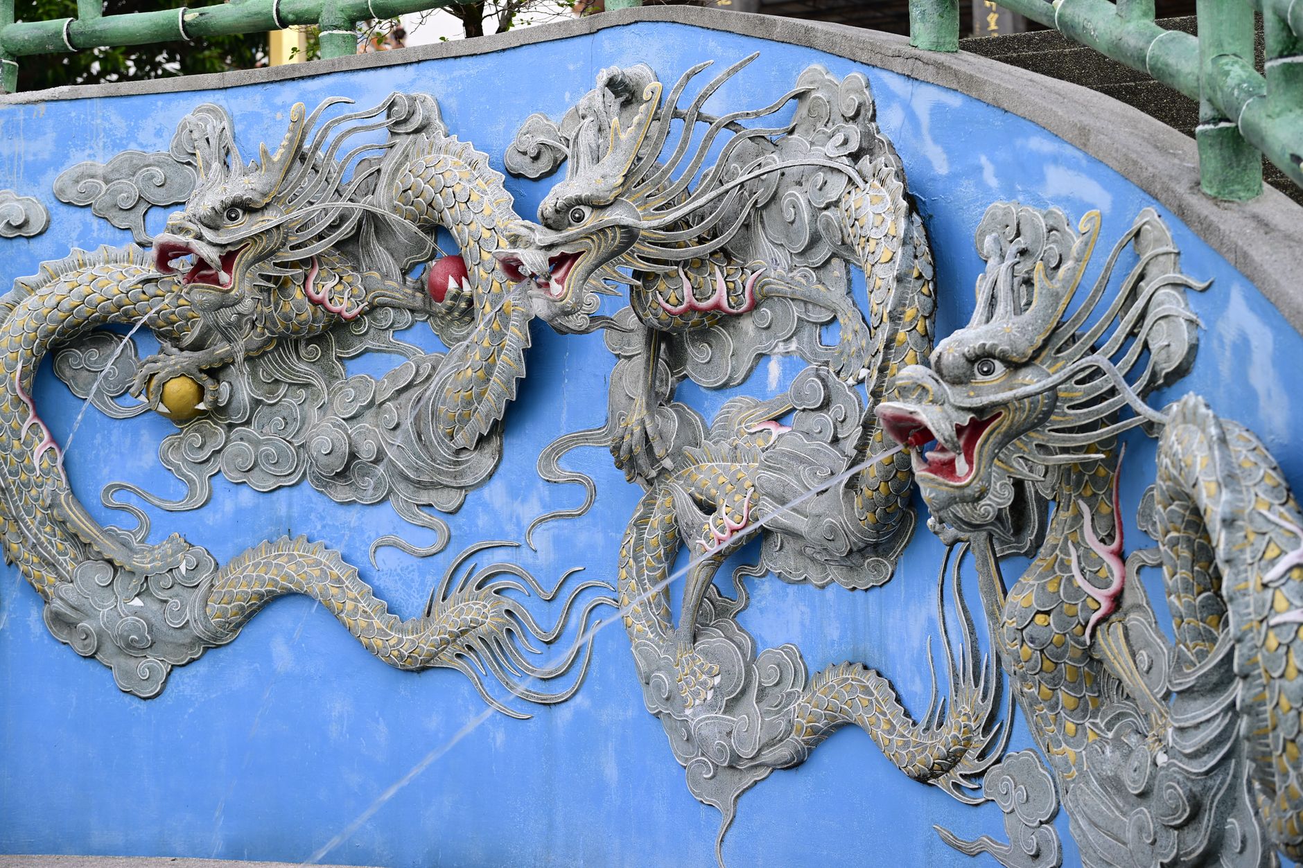 Detailed stone dragon sculpture on an ornate blue wall, outdoor setting.