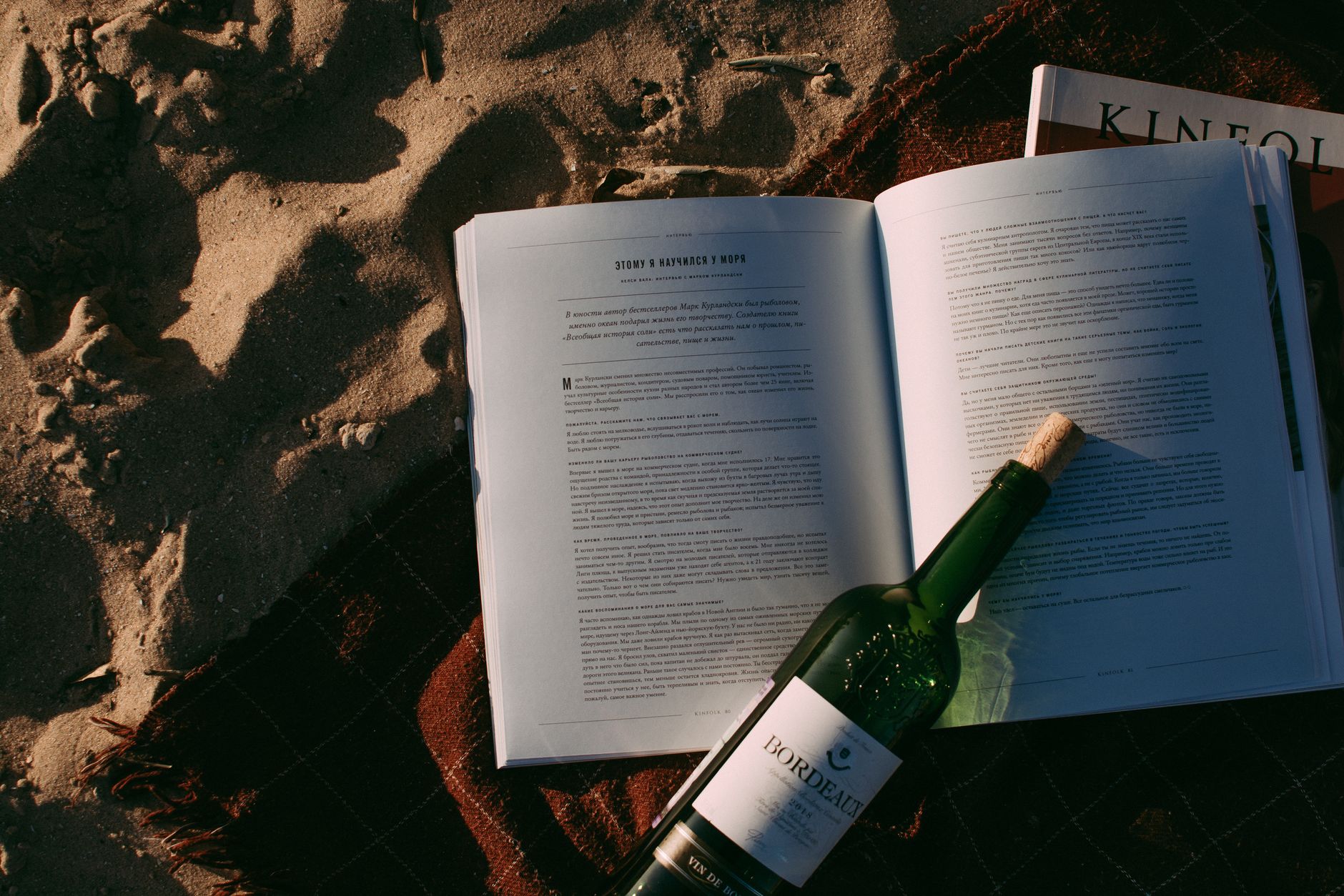 Open books and a Bordeaux bottle on the beach, ideal for leisure reading.