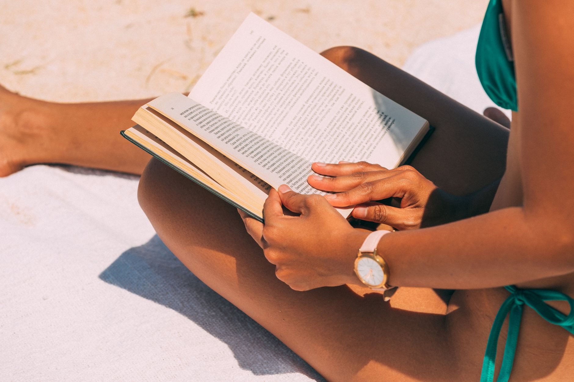 Close-up of a woman reading on a sandy beach in summer sunlight.