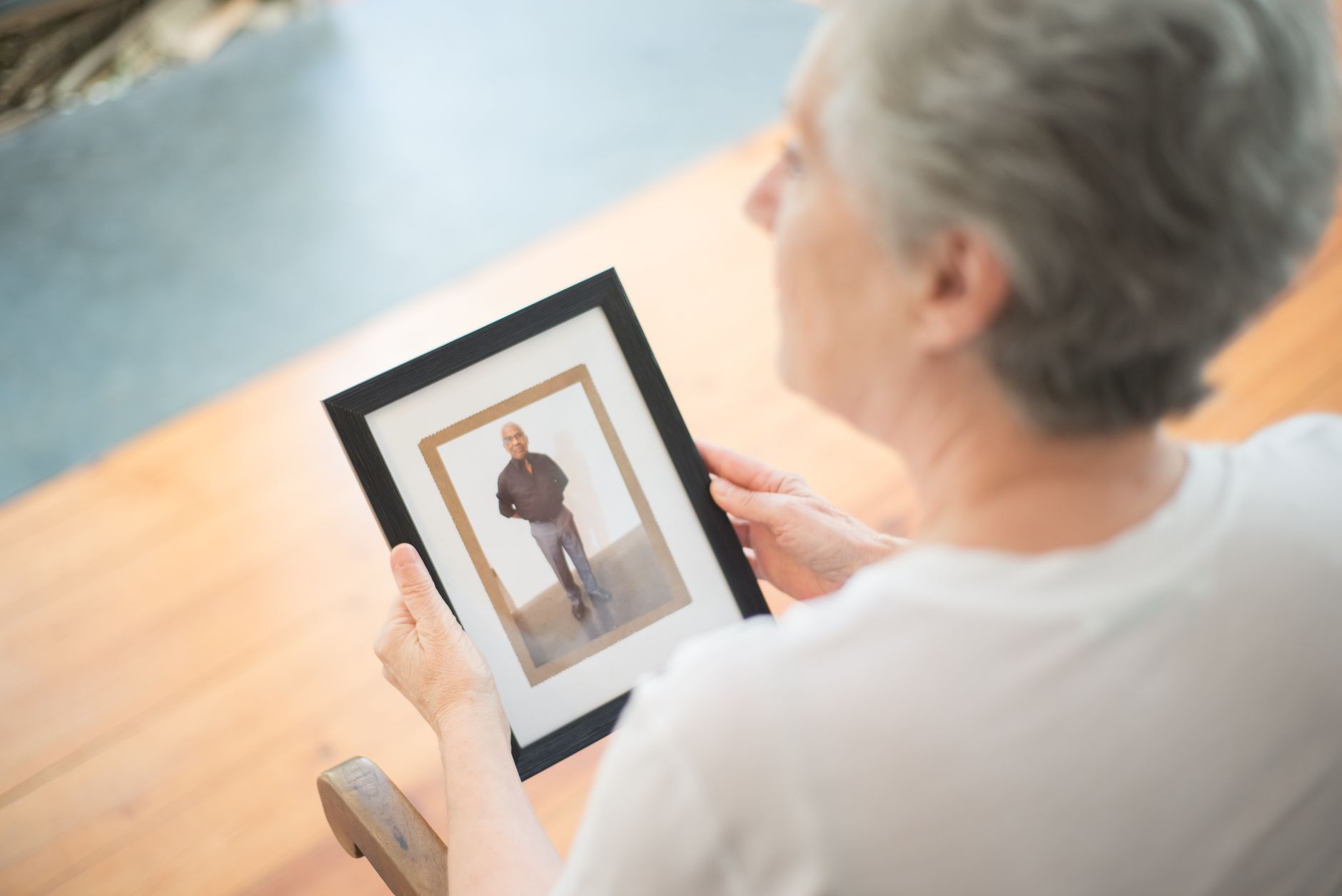Senior woman holding a framed picture, lost in memories, indoors.
