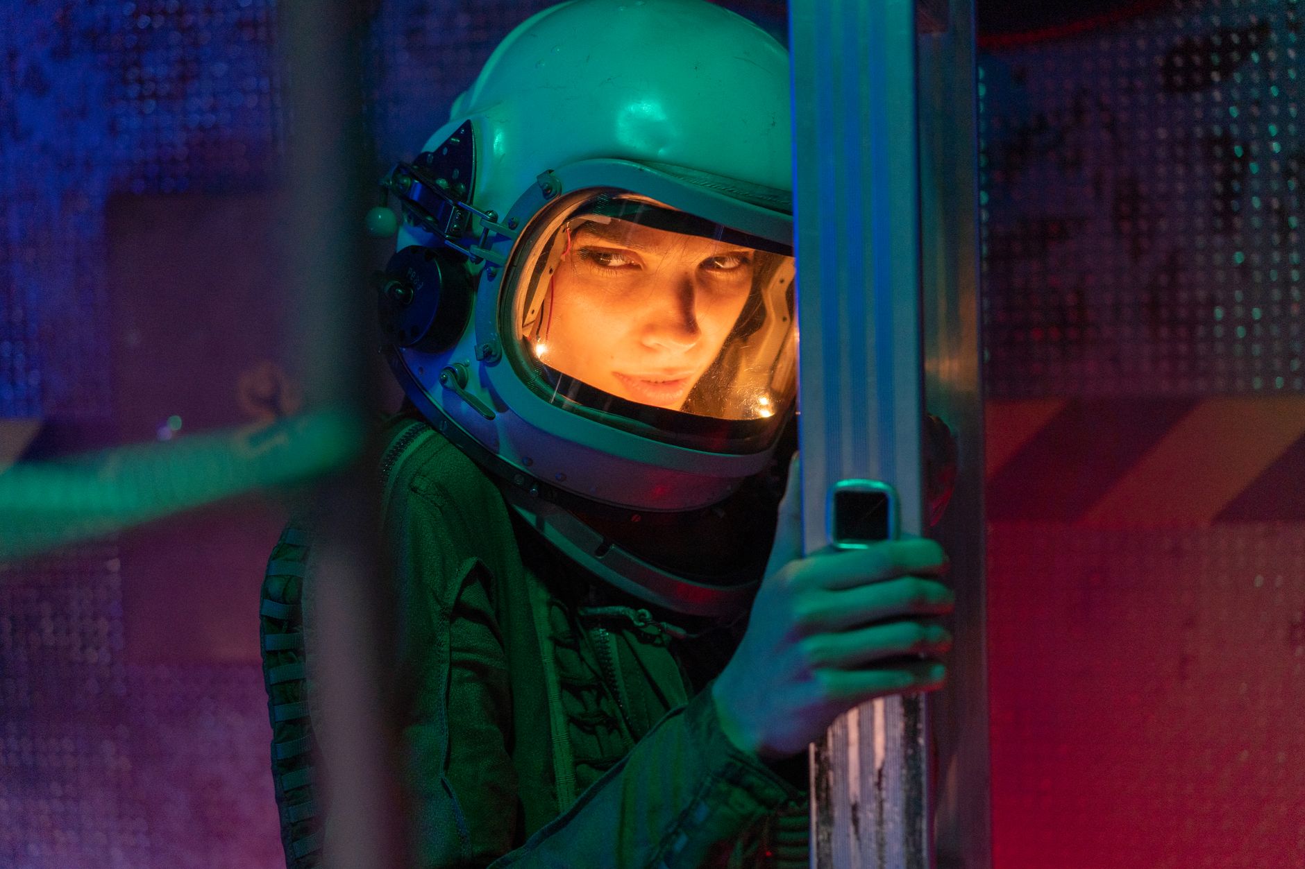 A woman astronaut in a helmet inside a sci-fi space vessel, surrounded by colorful lighting.