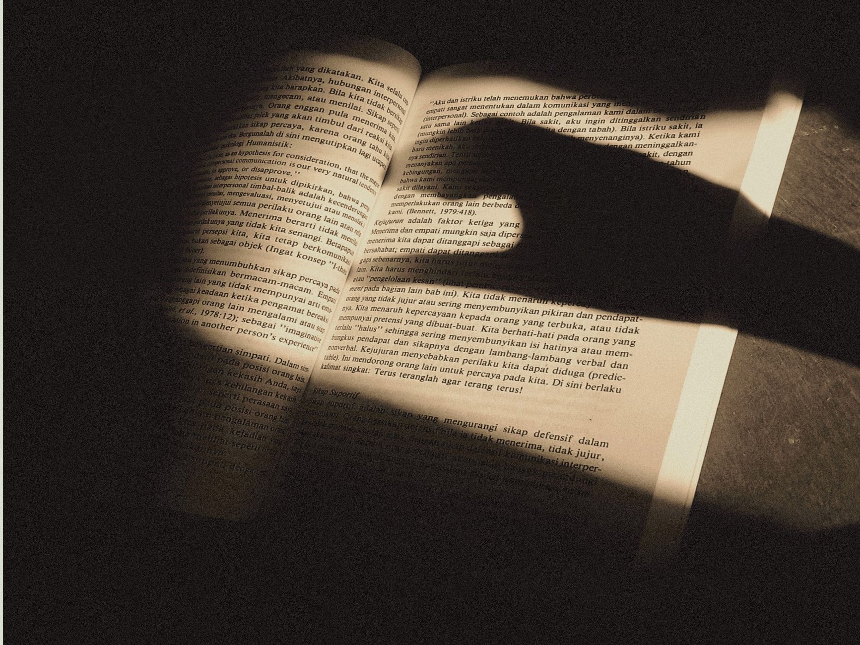 An open book with text illuminated by dramatic shadows, creating an intriguing visual effect.