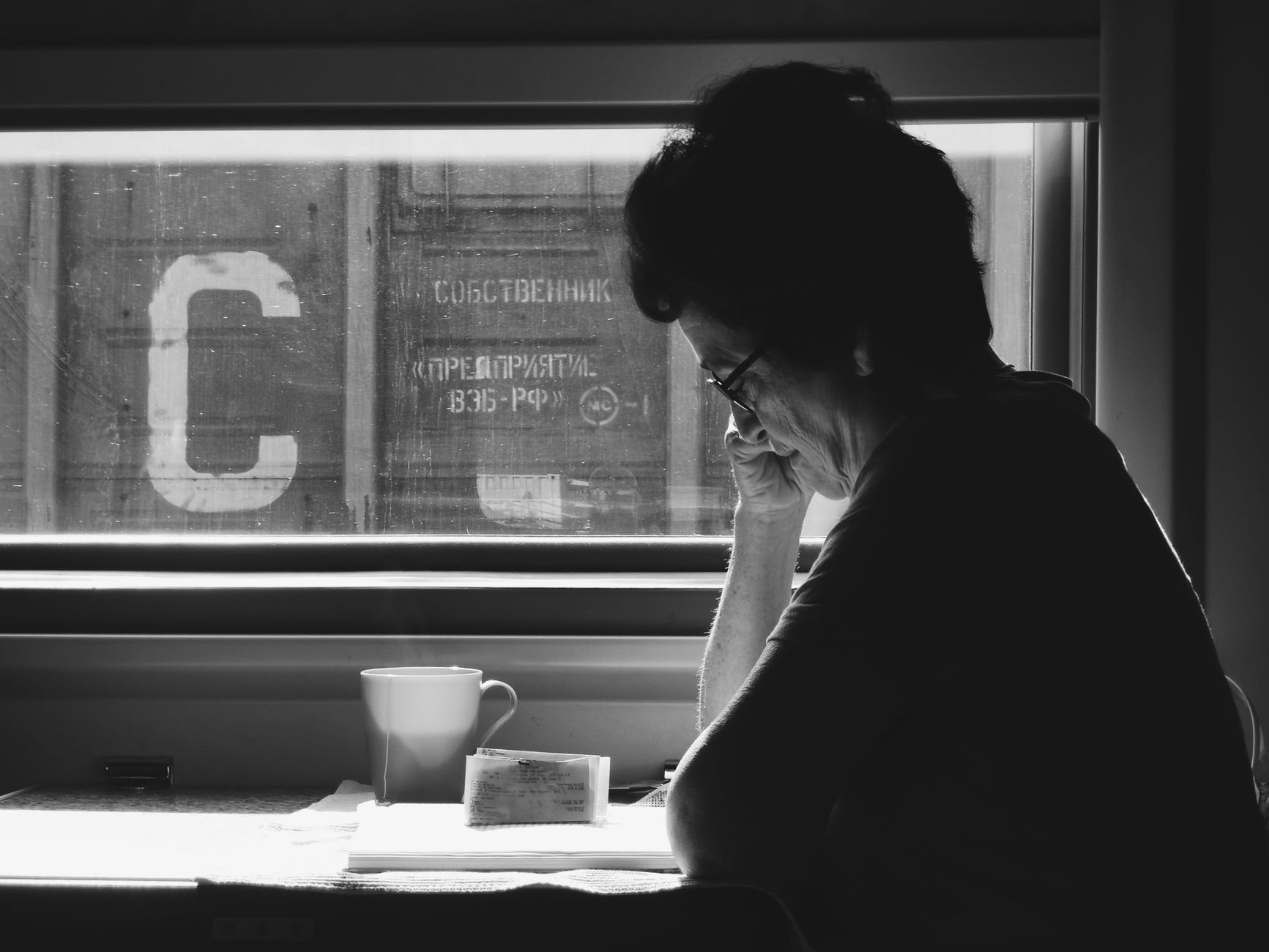 Black and white photo of a woman reading by a train window, serene and contemplative setting.