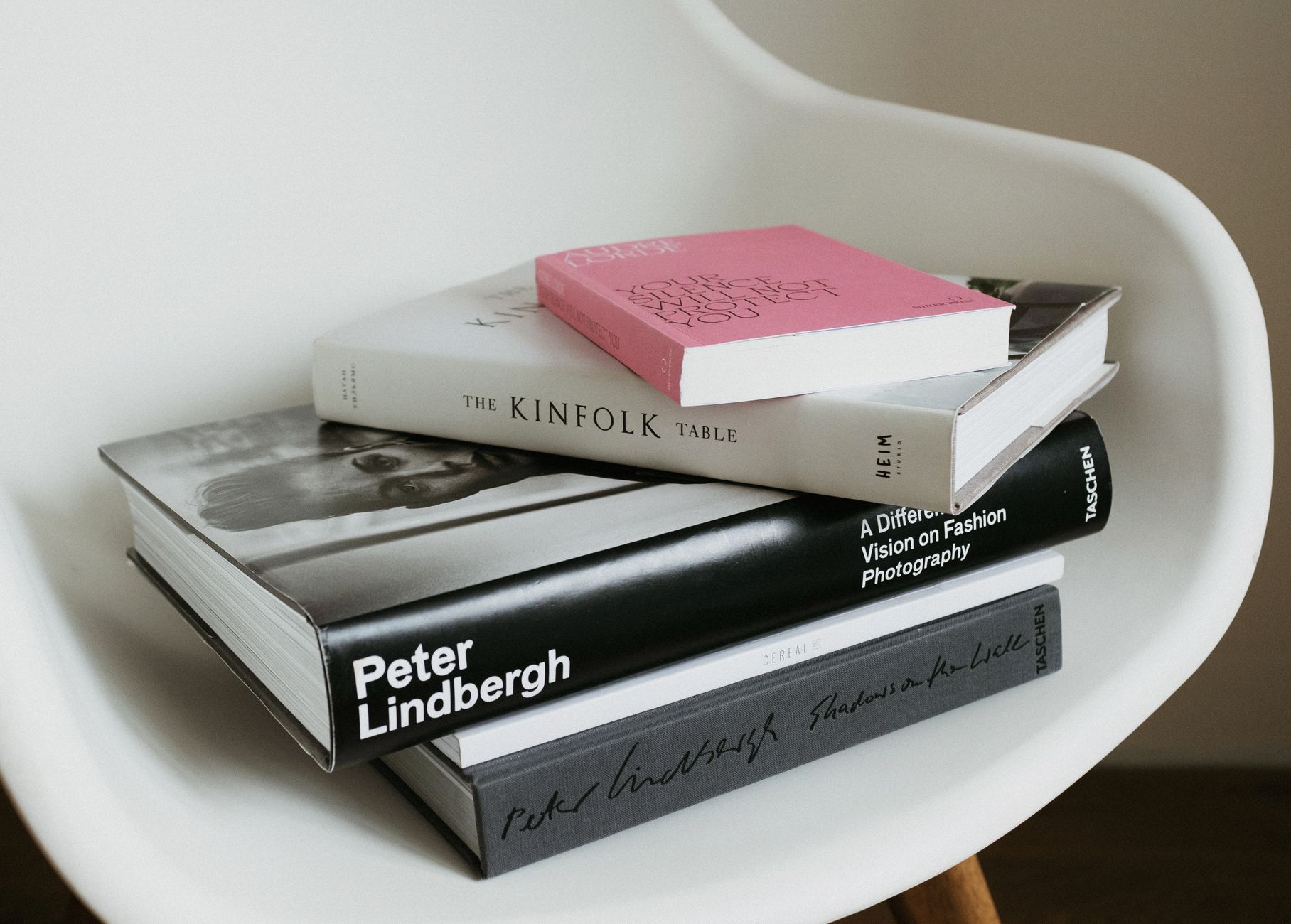 Arranged pile of modern art and fashion books from home collection placed on white chair near wall in modern light apartment