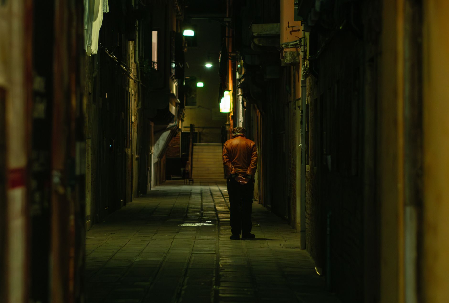 A senior man walks alone in a narrow alleyway in Venice, Italy, at night.