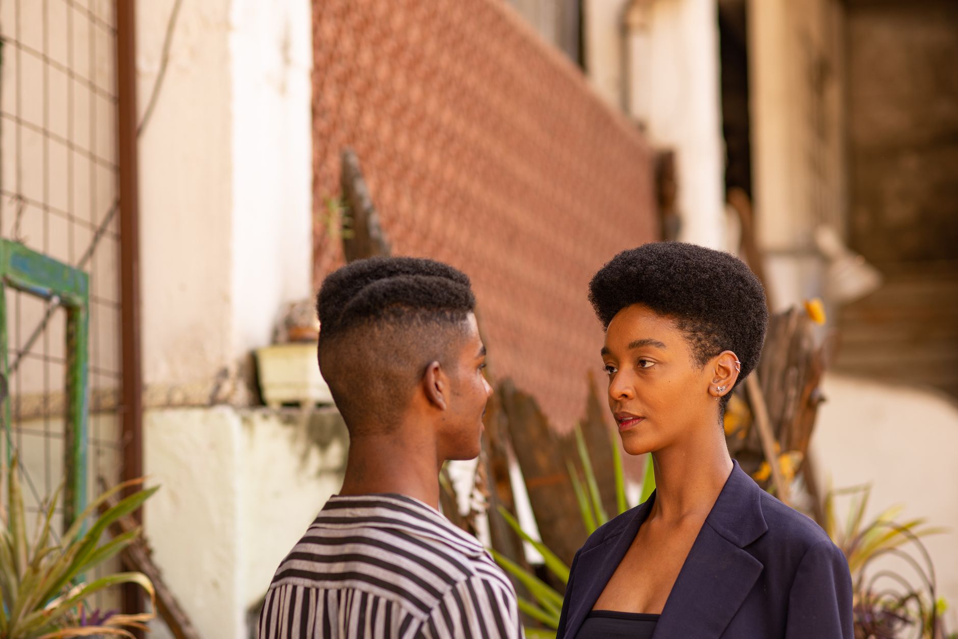 Young African American couple looking at each other while standing near shabby building on street of town against blurred background