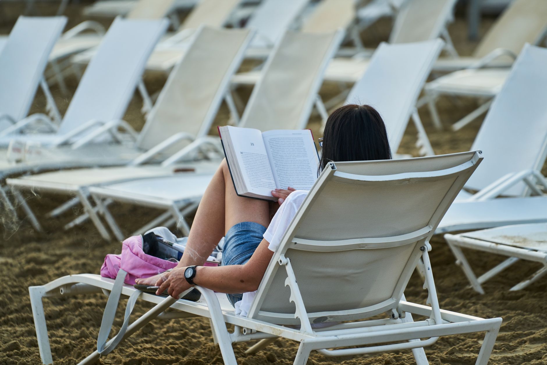 Woman reading a book on a lounge chair at the beach, enjoying a peaceful vacation day.