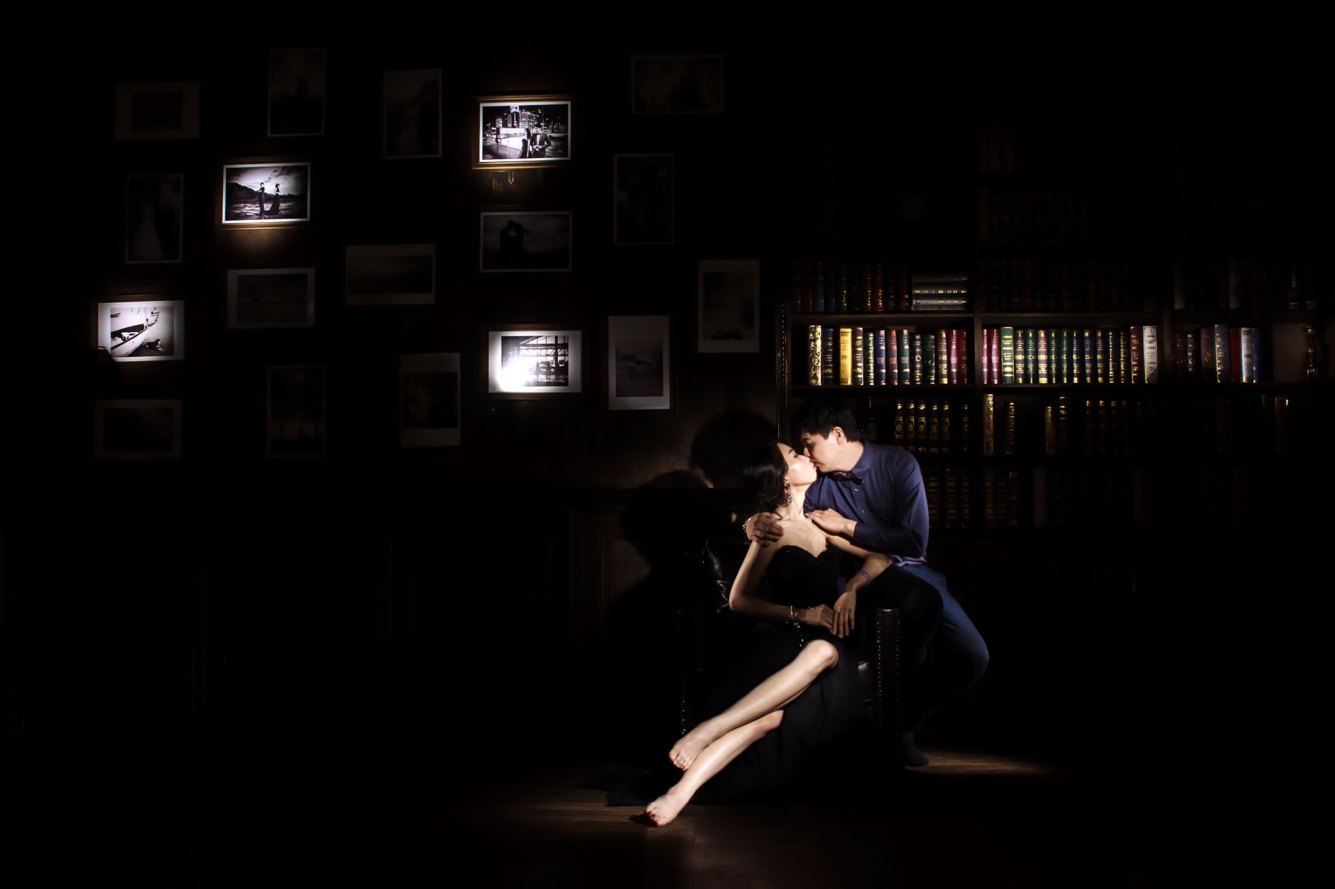 A romantic moment captured in a dark library with a couple kissing, surrounded by illuminated books and photos.