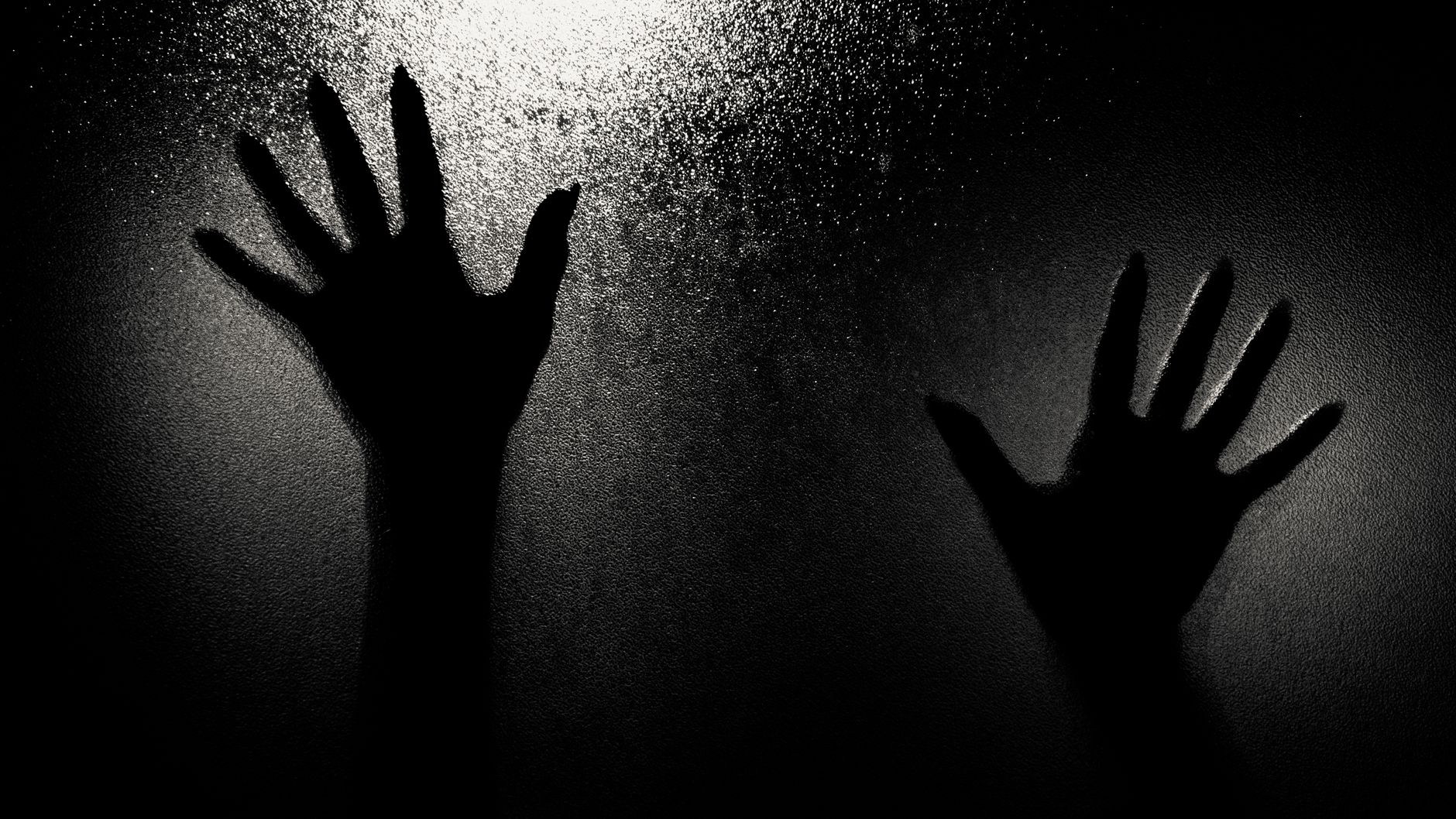 Dramatic silhouette of two hands pressed against a frosted glass, creating an eerie and mysterious ambiance.