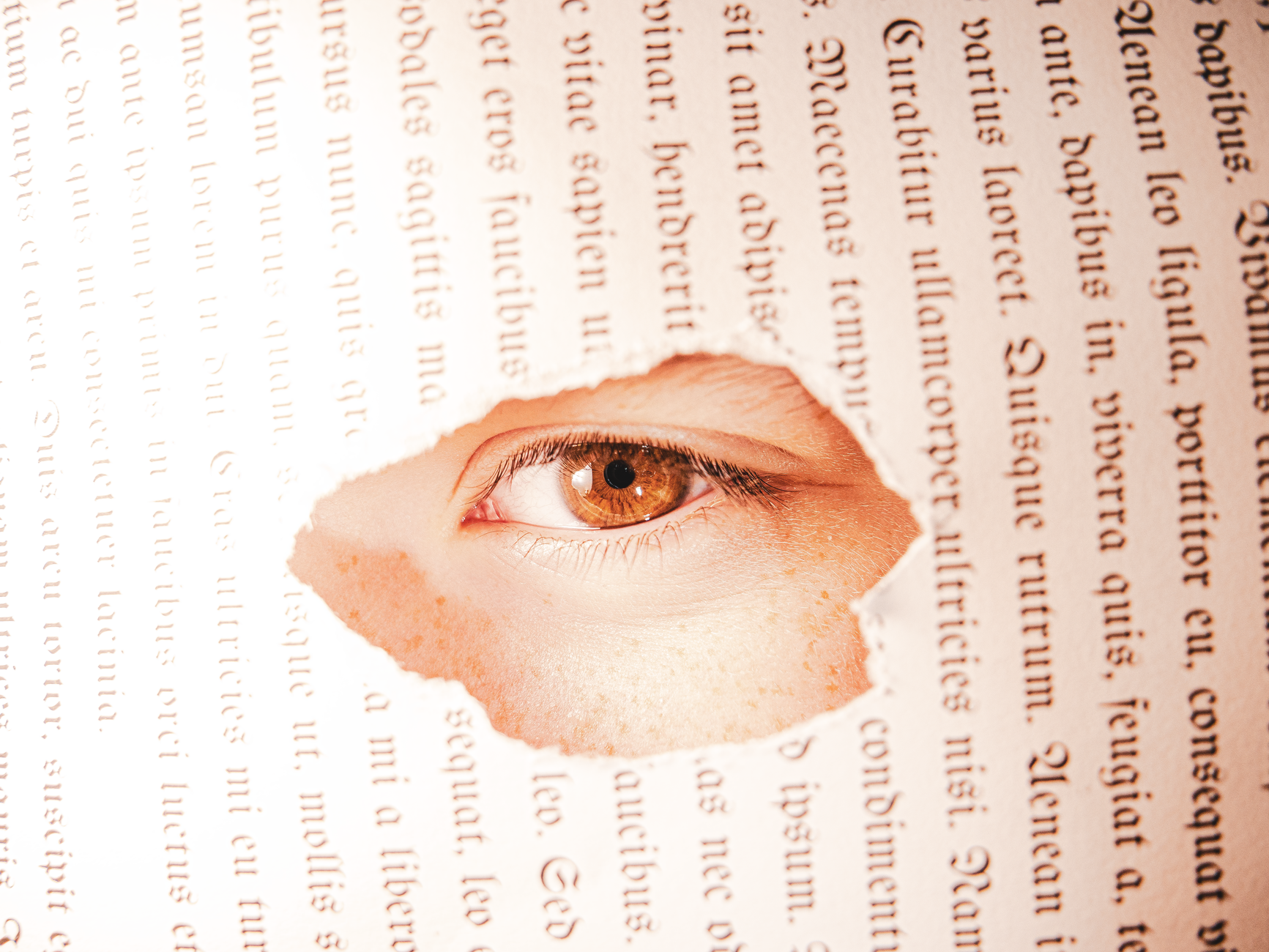 A close-up of an eye seen through a torn book page, creating a conceptual visual.