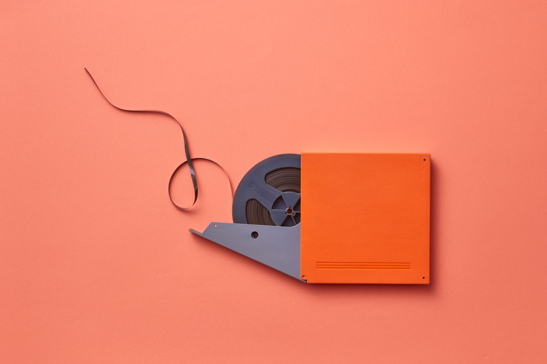 Close-up of a vintage film reel on a vibrant orange background with tape exposed.