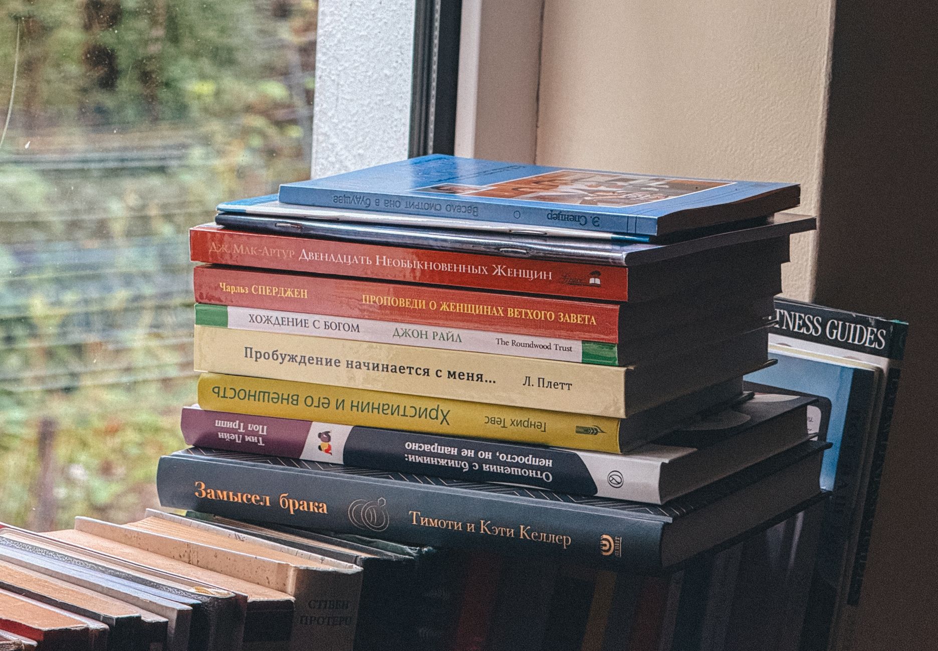 A stack of colorful books by a window, creating a cozy and intellectual atmosphere indoors.