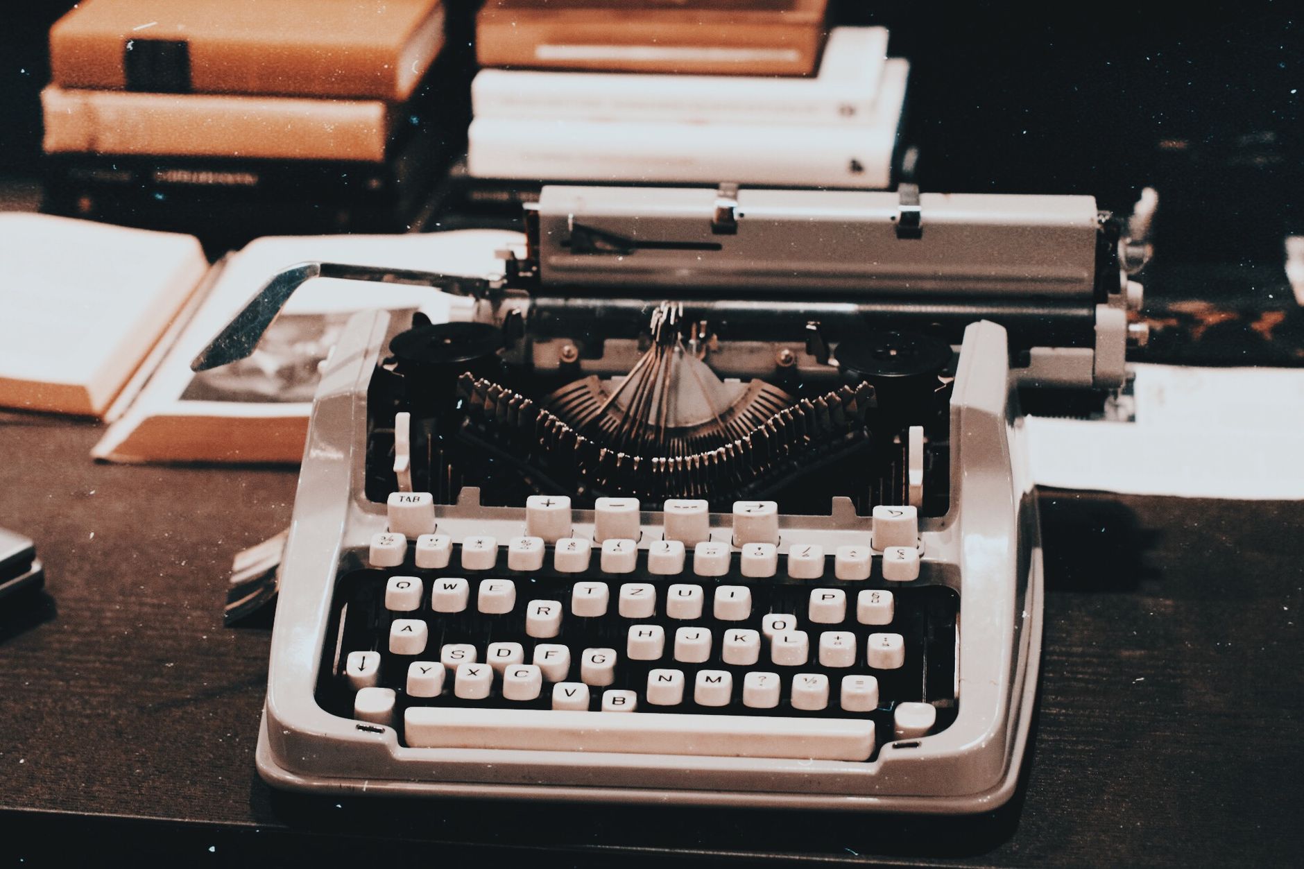 Close-up of an antique typewriter on a desk surrounded by books, evoking a classic retro style.