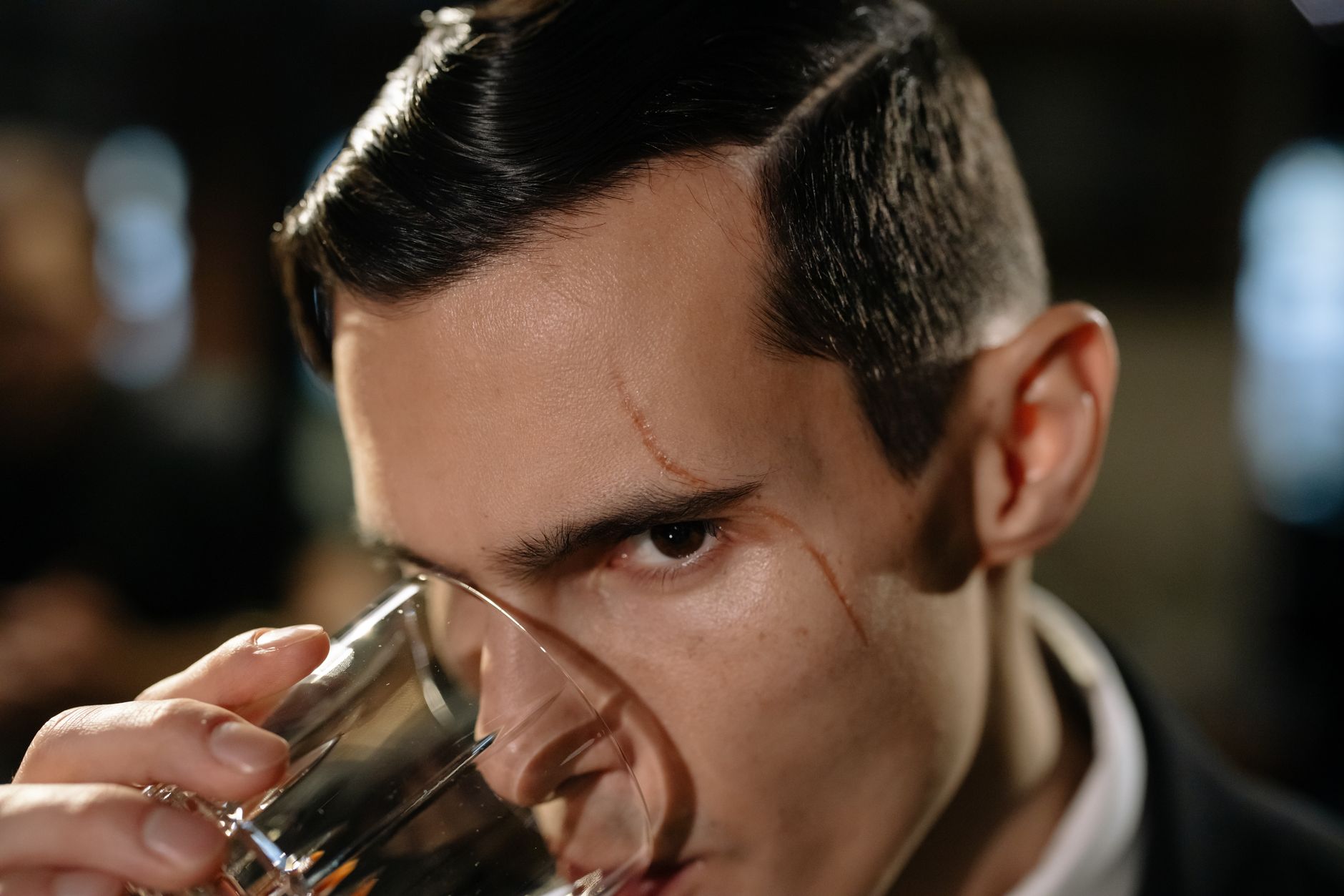 Close-up of a mysterious scarred man holding a glass, creating a noir atmosphere.