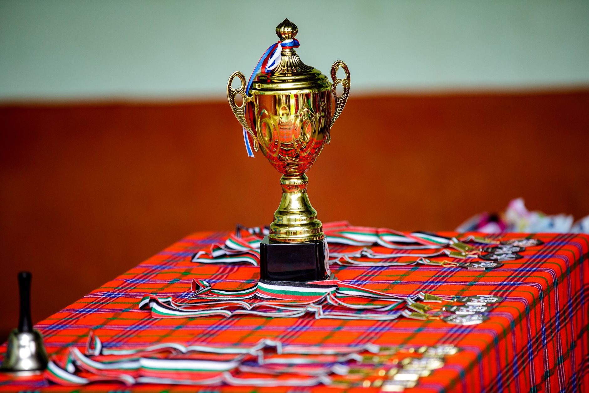 Golden trophy with ribbons and medals on a checkered table, symbolizing victory and achievement.