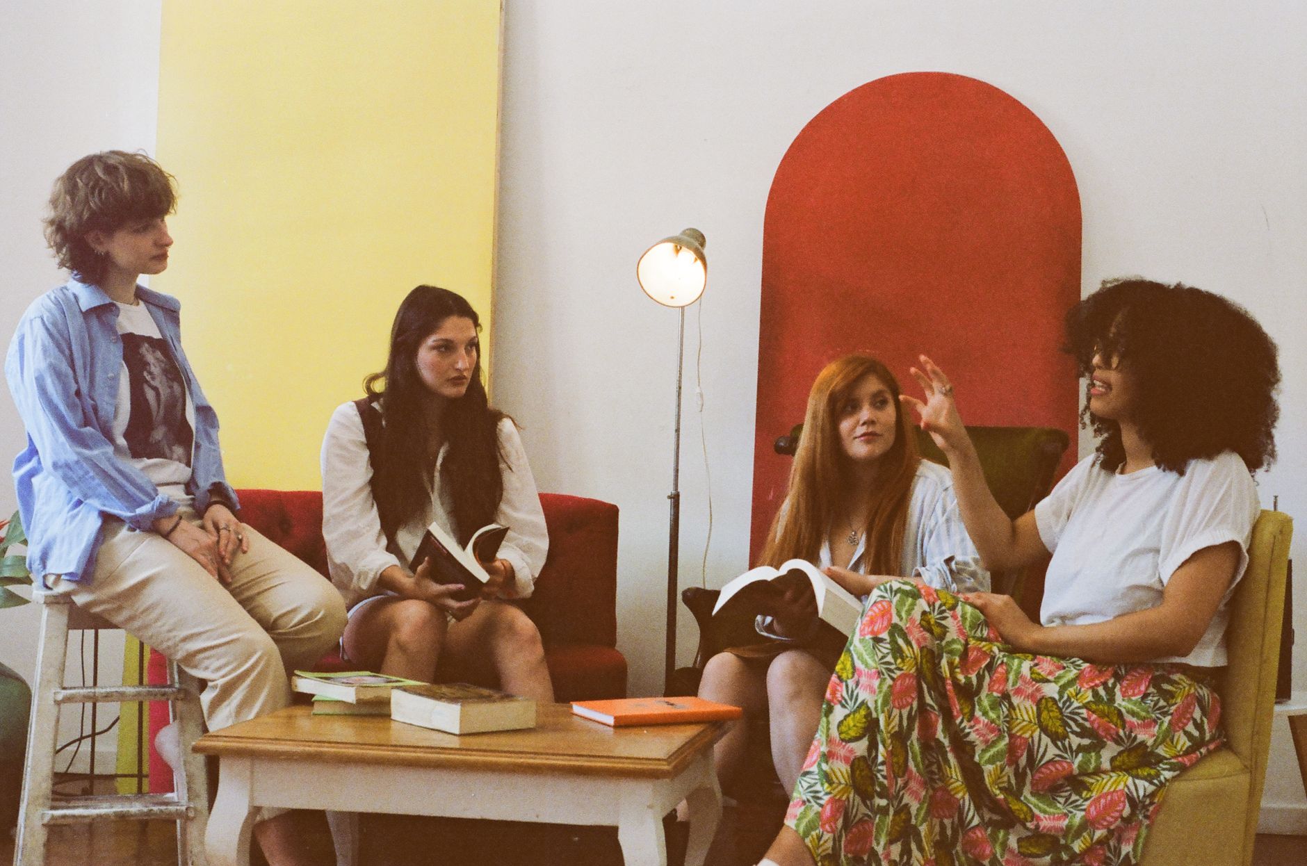 A group of four women casually discussing books in a cozy, colorful room.