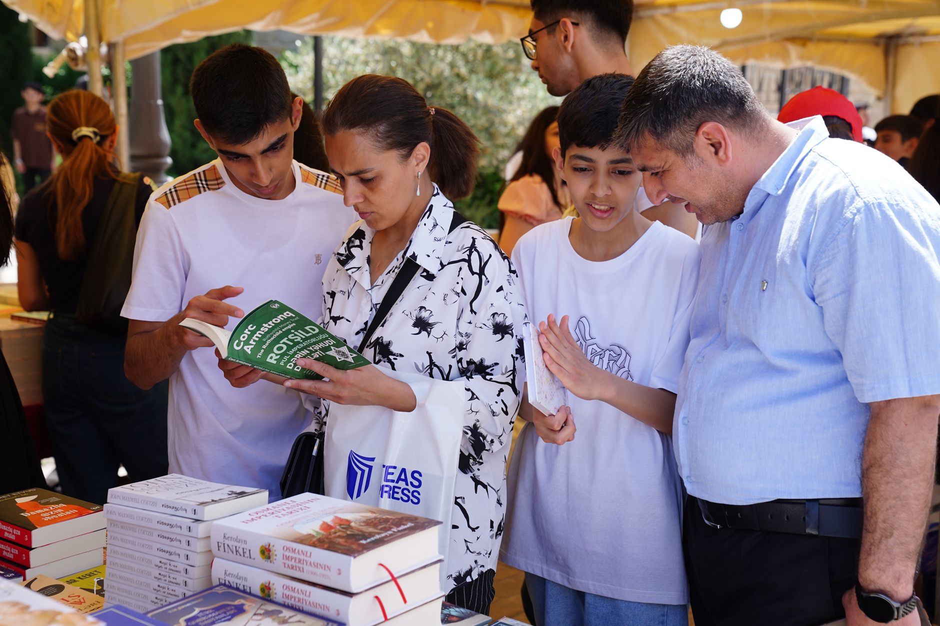 Family exploring books together at an outdoor book fair under a sunny day tent.