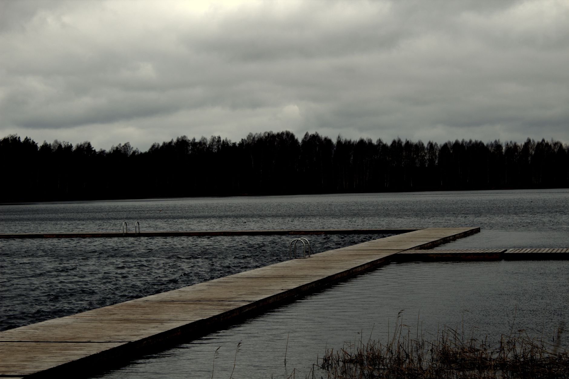 A solitary wooden pier stretches into a vast lake, framed by overcast skies and dense forests.