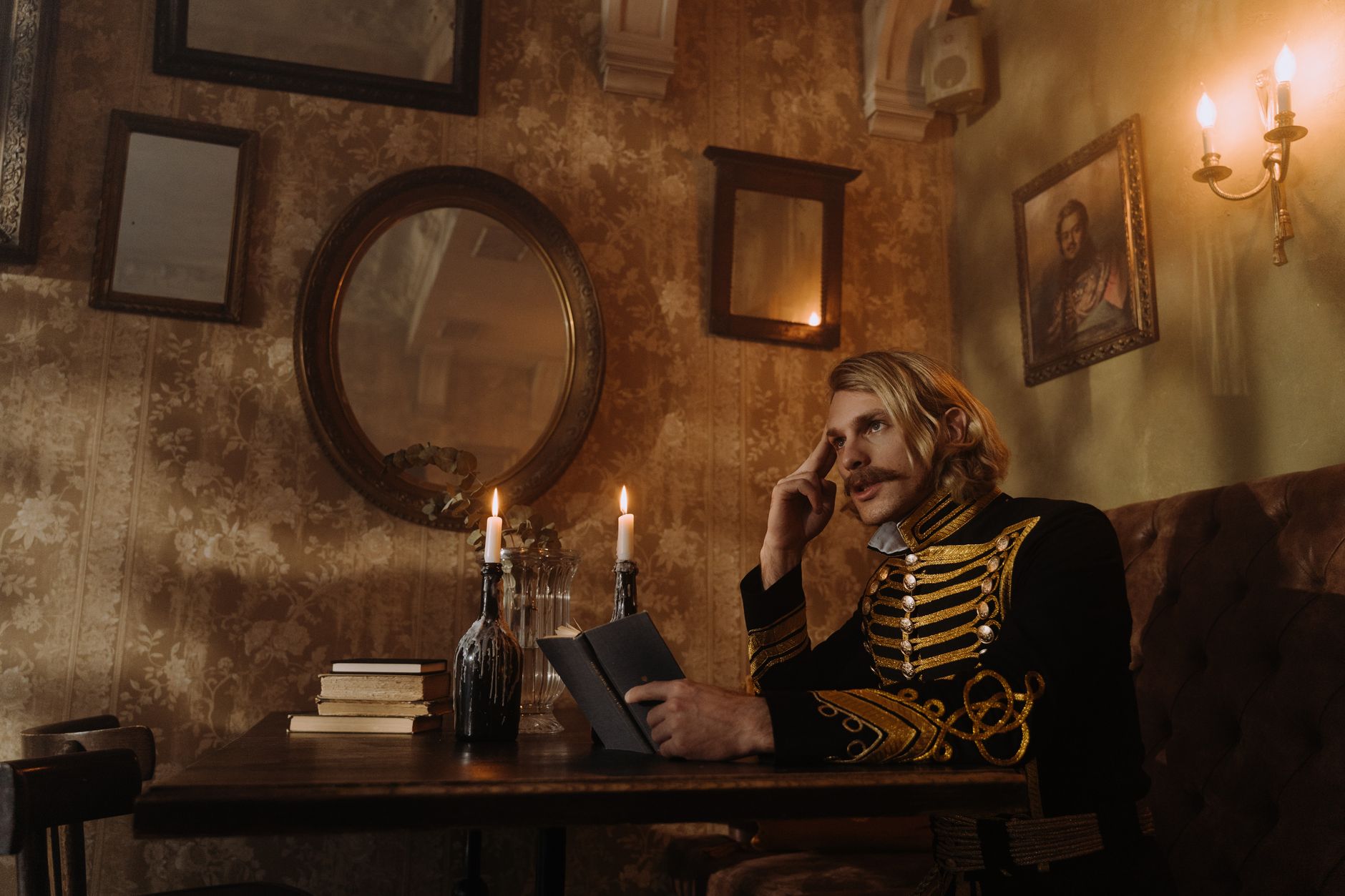 A man in Russian officer attire seated at a table with books and candles in a vintage setting.