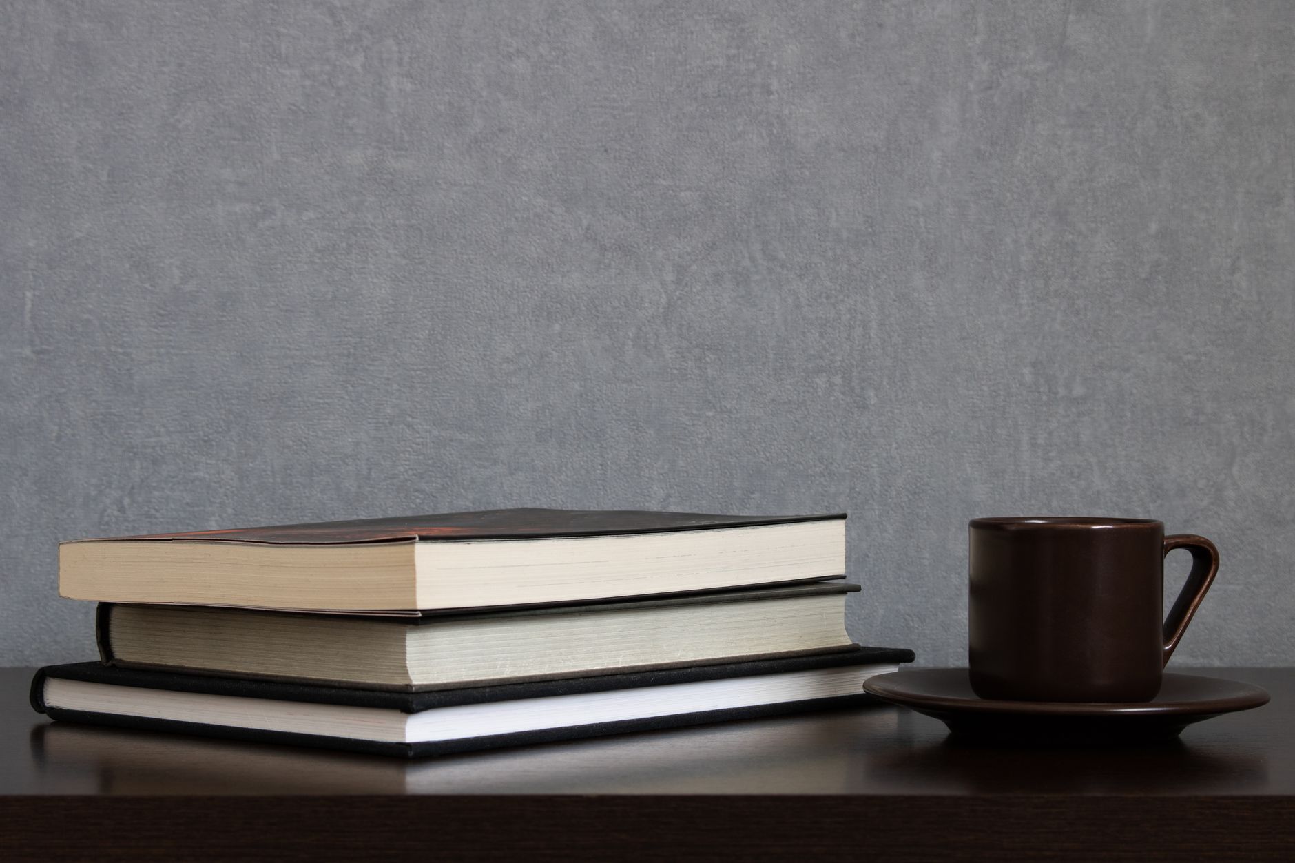 A stack of books next to a coffee cup on a wooden table, perfect for study or relaxation.