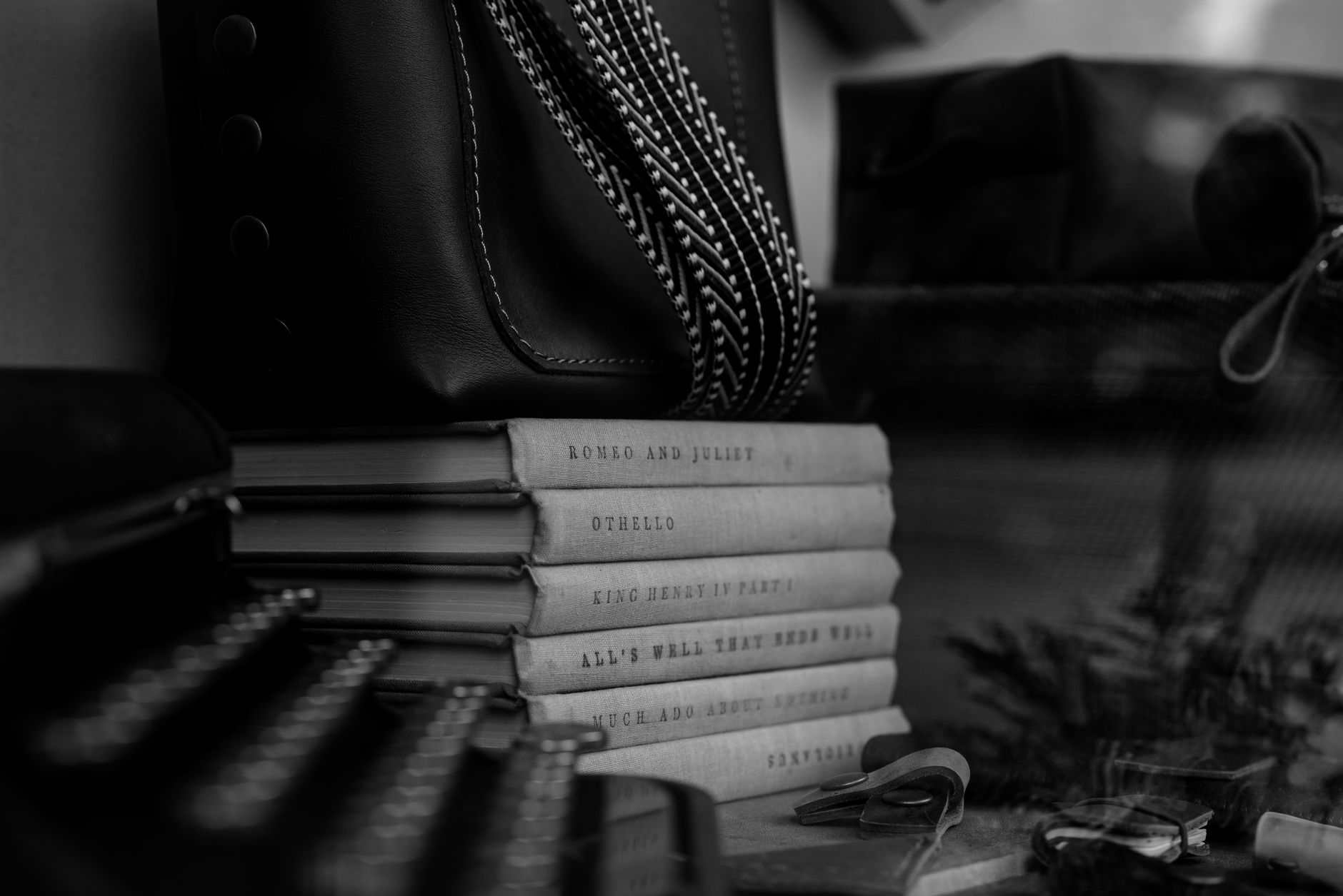 Monochrome photo of classic books stacked with a typewriter and leather bag.