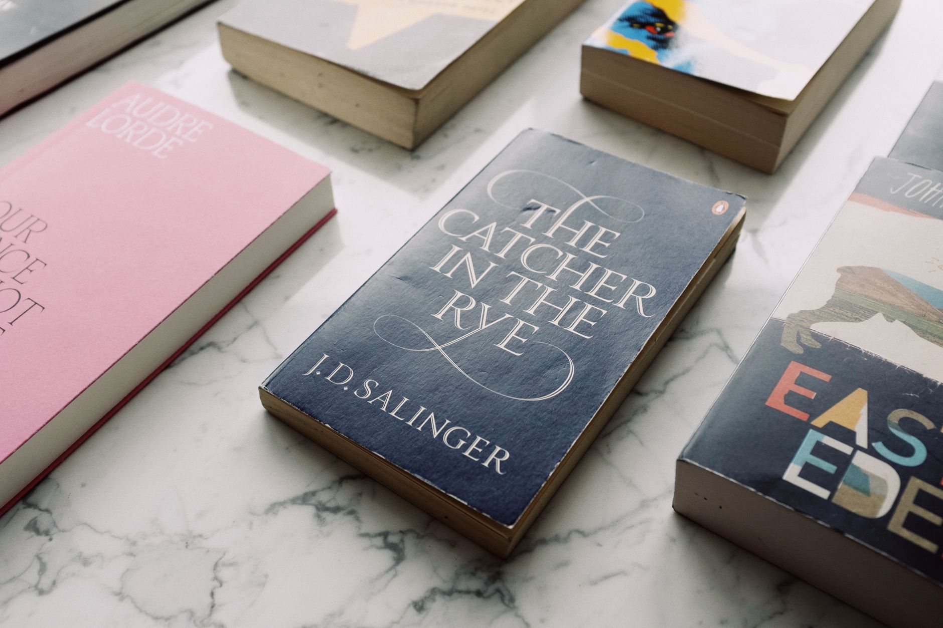 A collection of classic novels displayed on a marble surface, showcasing titles like 'The Catcher in the Rye.'