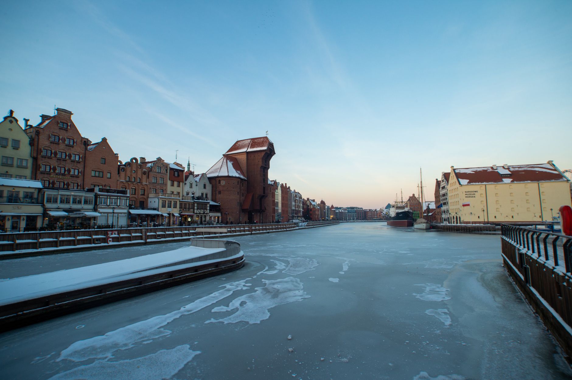 Scenic winter view of the frozen Motława River in Gdansk, highlighting traditional architecture and icy waters.
