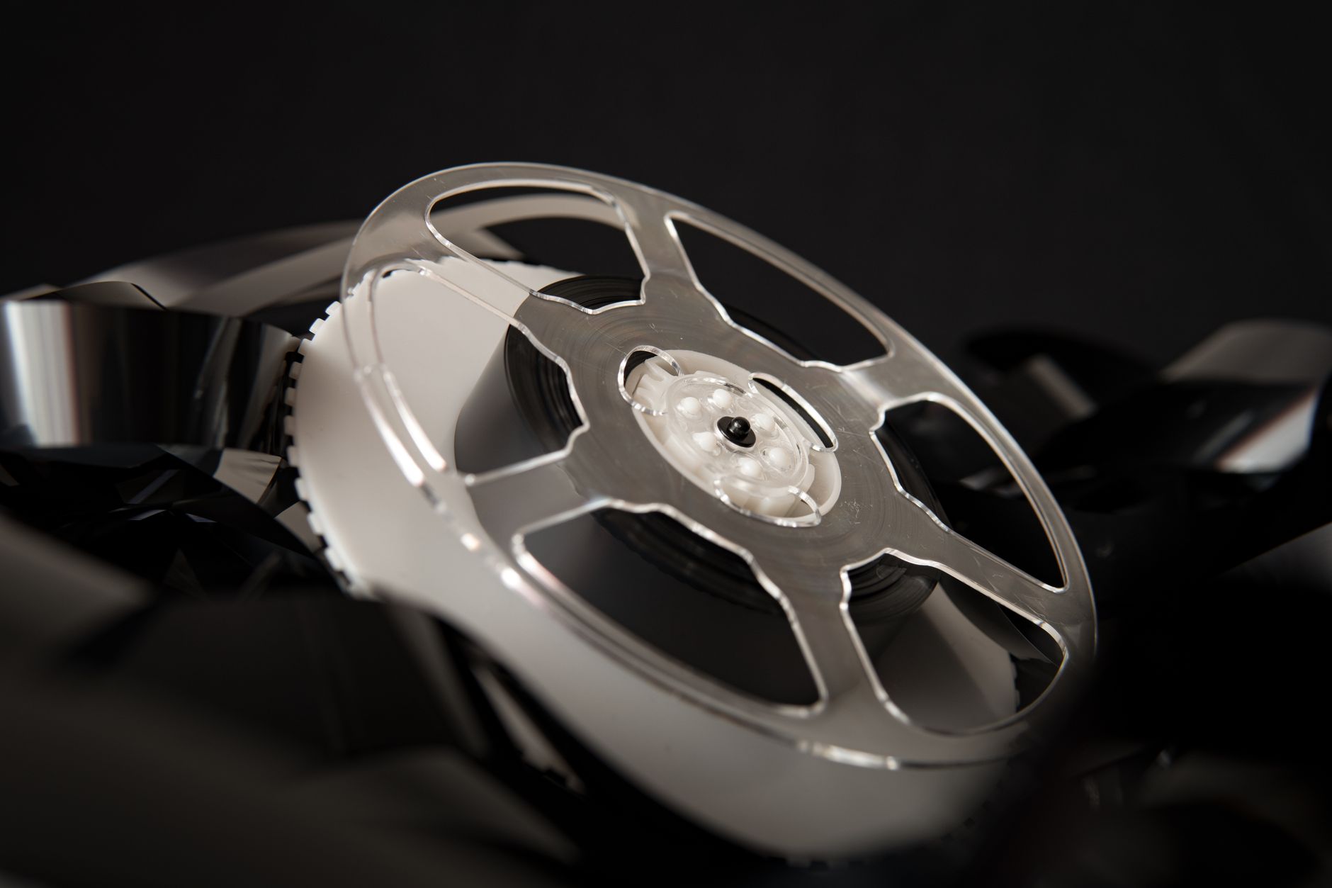 Transparent plastic bobbin placed on pile of unrolled film for movie production on black background